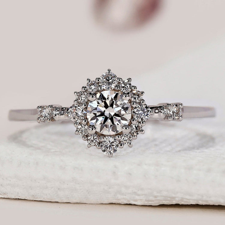 Halo engagement ring with round diamond and side stones in white gold.
