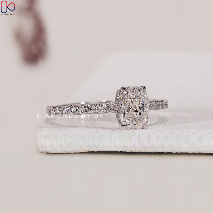 Handmade Jewellery featuring a cushion diamond center stone with round side diamonds, set in a pave band and hidden halo.
