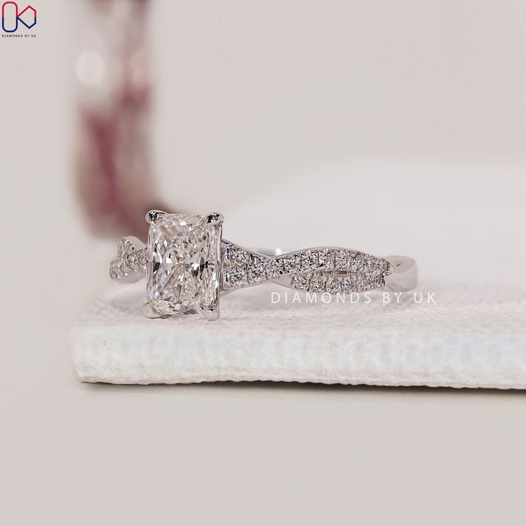 Twisted Band Cushion Cut Diamond Ring with 4 prong claw setting and round side diamonds, made in white gold.

