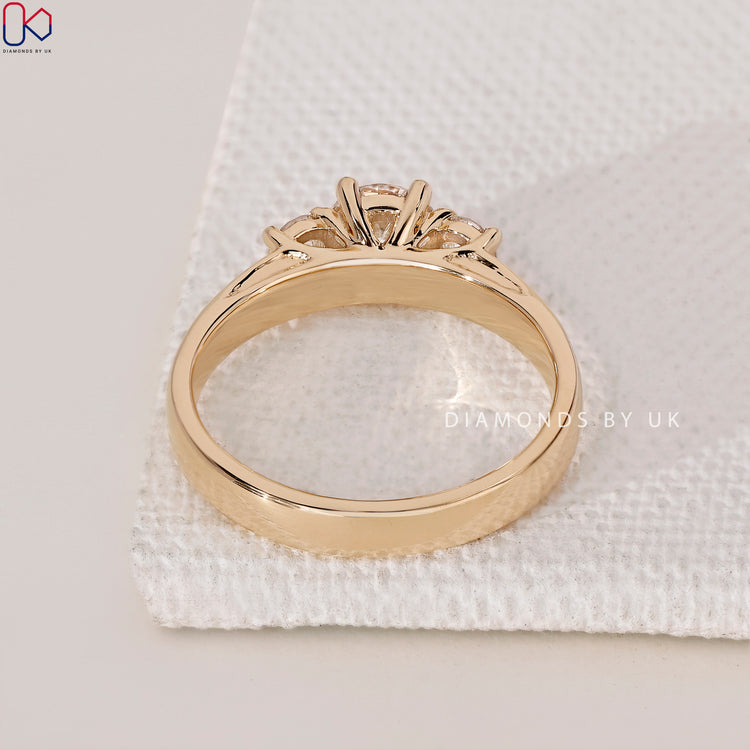 Engagement Ring UK featuring three round diamonds in a wide yellow gold band.
