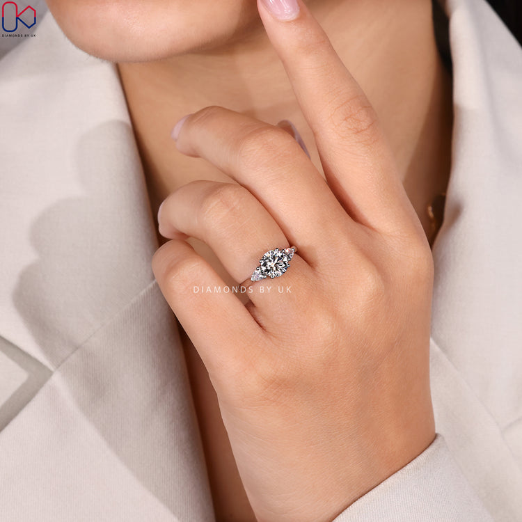 Round diamond ring with pear side stones and prongs.