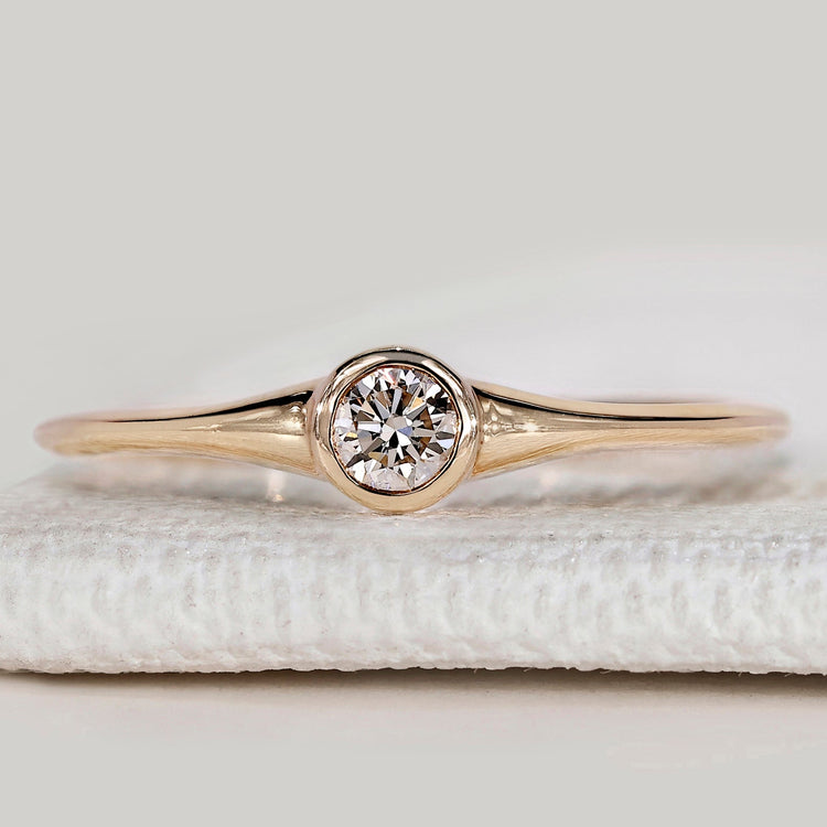Minimalist round diamond ring with bezel setting.
