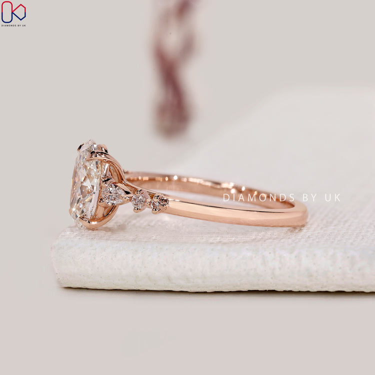 Rose gold engagement ring with oval and side stones.

