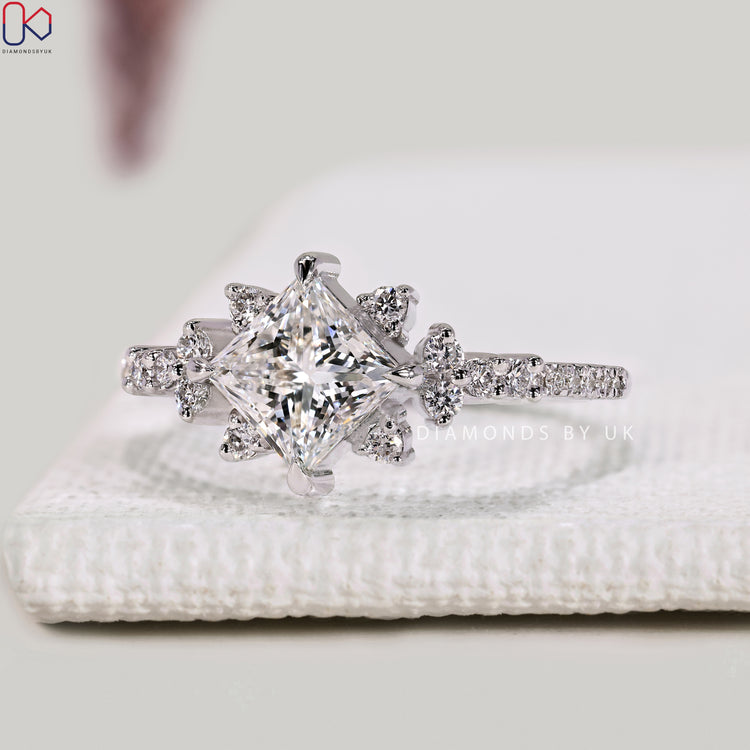 Princess diamond ring with side stones and compass prongs.
